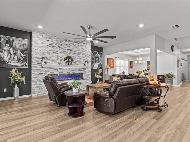 living room featuring ceiling fan with notable chandelier, light hardwood / wood-style flooring, and a tiled fireplace