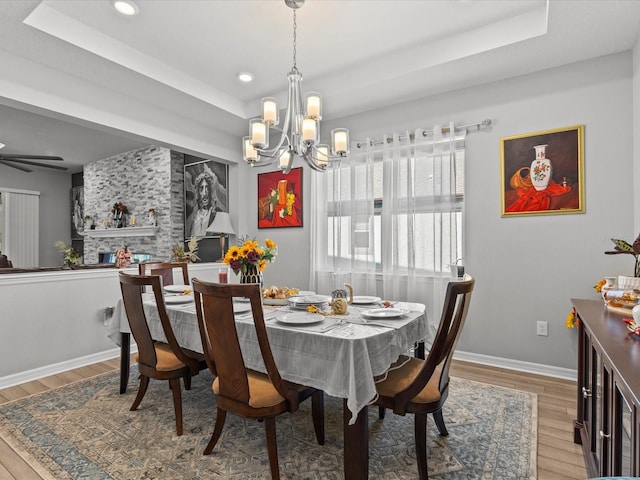 dining area featuring ceiling fan with notable chandelier, hardwood / wood-style flooring, and a tray ceiling