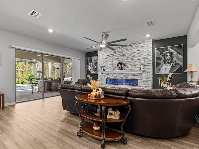 living room featuring ceiling fan, a fireplace, light hardwood / wood-style floors, and a textured ceiling