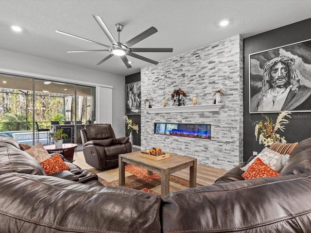 living room with hardwood / wood-style floors, ceiling fan, a stone fireplace, and a textured ceiling