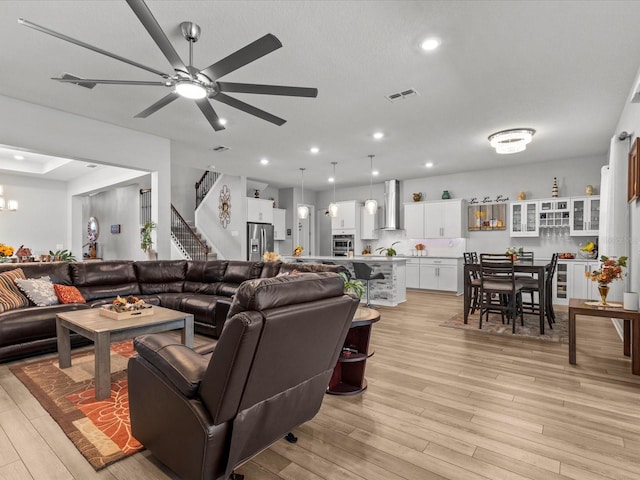 living room featuring ceiling fan with notable chandelier, a textured ceiling, and light wood-type flooring