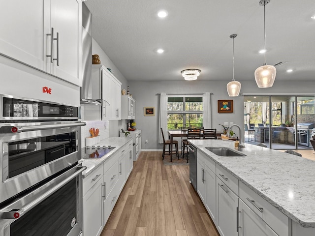 kitchen with stainless steel appliances, a kitchen island with sink, sink, light hardwood / wood-style flooring, and white cabinetry