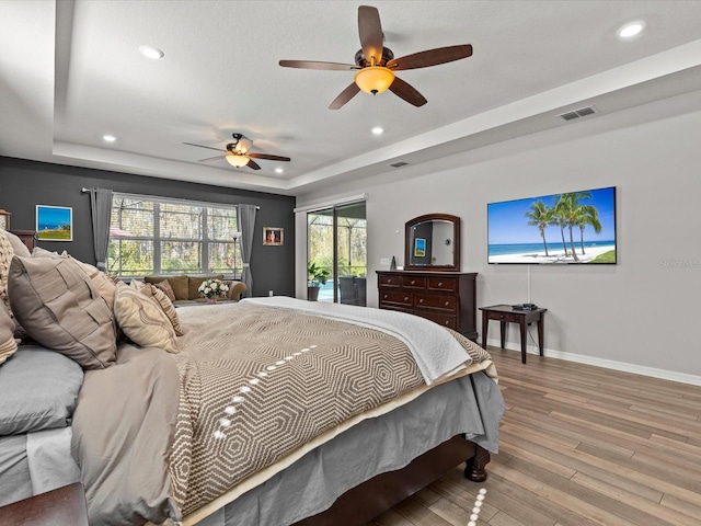 bedroom featuring access to outside, hardwood / wood-style flooring, a raised ceiling, and ceiling fan