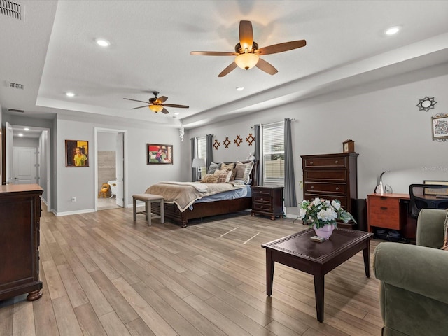 bedroom with a raised ceiling, ensuite bath, ceiling fan, and light hardwood / wood-style floors