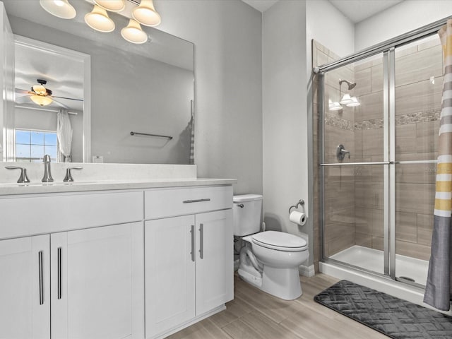 bathroom featuring ceiling fan, toilet, a shower with door, vanity, and hardwood / wood-style flooring