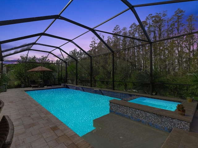 pool at dusk with glass enclosure and a patio