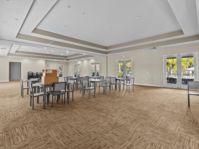 carpeted dining area featuring french doors, a raised ceiling, and a healthy amount of sunlight