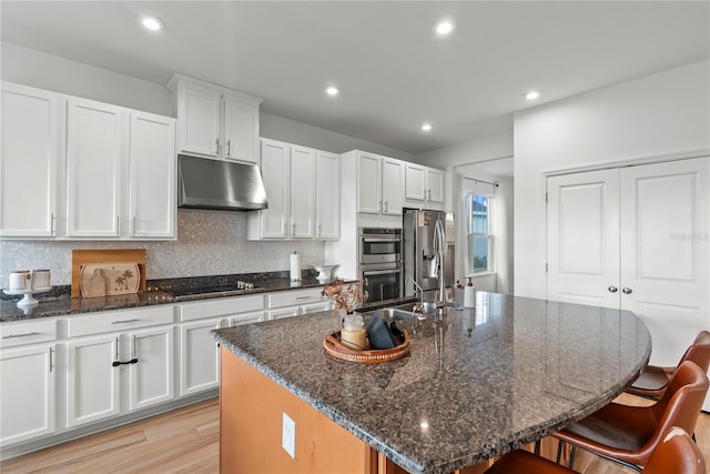 kitchen featuring a center island with sink, white cabinets, sink, dark stone countertops, and appliances with stainless steel finishes