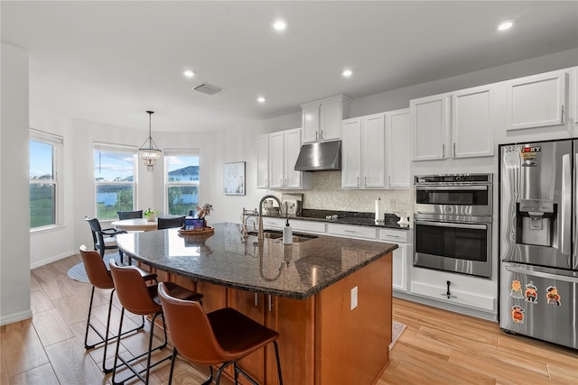 33975 Astoria Cir, Wesley Chapel, FL 33545 - kitchen featuring appliances with stainless steel finishes, under cabinet range hood, a kitchen island with sink, a kitchen breakfast bar, and white cabinets