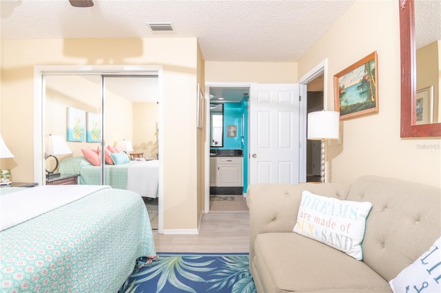 bedroom with ceiling fan, a textured ceiling, light hardwood / wood-style floors, and a closet