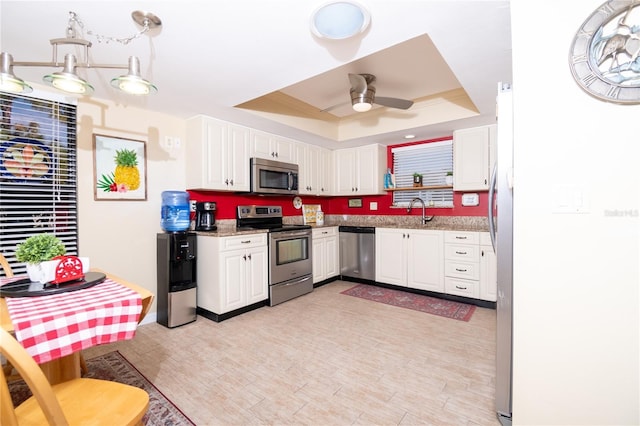 kitchen featuring appliances with stainless steel finishes, a raised ceiling, ceiling fan, light stone countertops, and white cabinets