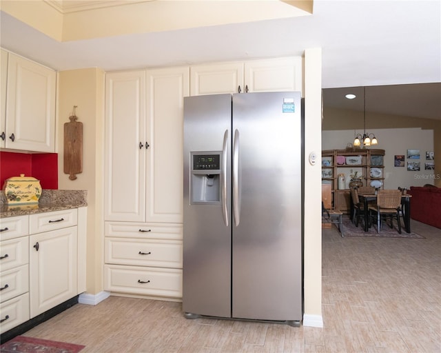 kitchen featuring stainless steel fridge, an inviting chandelier, hanging light fixtures, light hardwood / wood-style floors, and dark stone counters