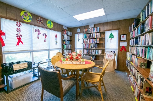 playroom with carpet flooring, a paneled ceiling, and wood walls