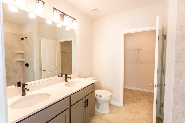 bathroom featuring tile patterned flooring, a tile shower, vanity, and toilet