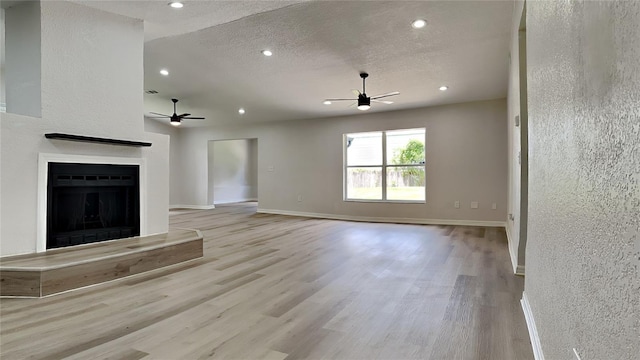 unfurnished living room with a textured ceiling, light hardwood / wood-style flooring, and ceiling fan