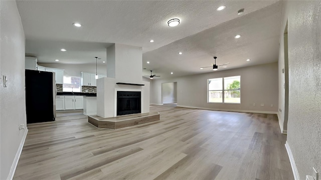 unfurnished living room featuring light wood-type flooring, a textured ceiling, ceiling fan, sink, and lofted ceiling