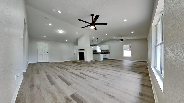 unfurnished living room with a textured ceiling, light hardwood / wood-style floors, vaulted ceiling, and ceiling fan