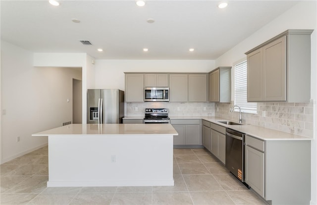 kitchen featuring gray cabinetry, stainless steel appliances, a kitchen island, a sink, and visible vents