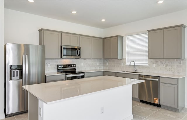 kitchen with stainless steel appliances, tasteful backsplash, gray cabinetry, a sink, and a kitchen island