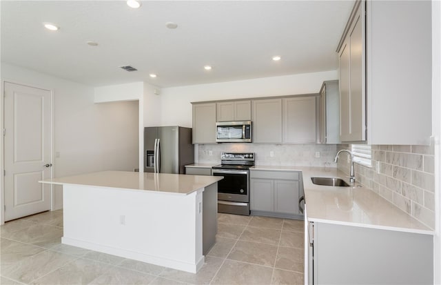 kitchen featuring decorative backsplash, a center island, stainless steel appliances, gray cabinetry, and a sink