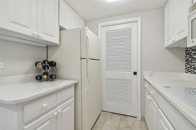 kitchen with a textured ceiling, white cabinetry, light stone countertops, and white appliances