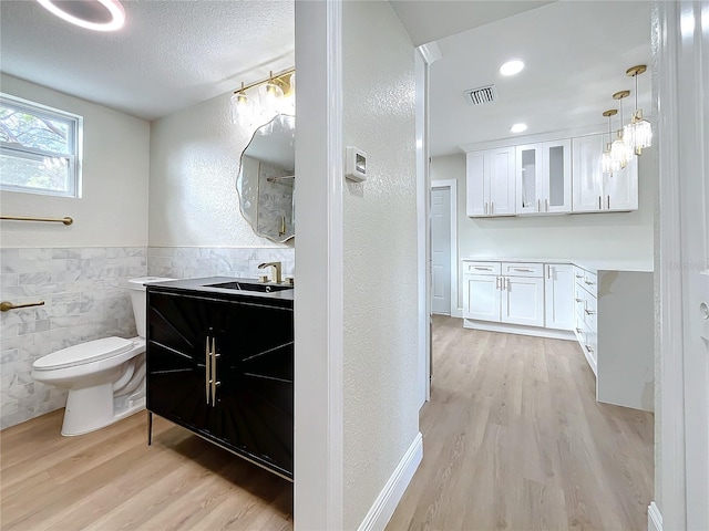 bathroom with wood-type flooring, vanity, toilet, and tile walls