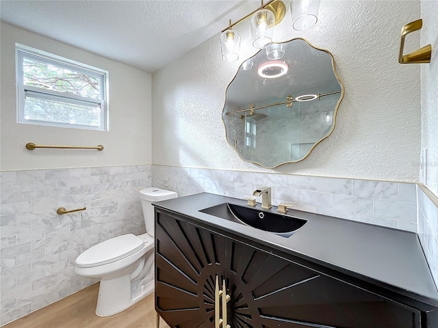 bathroom featuring hardwood / wood-style floors, a textured ceiling, toilet, vanity, and tile walls