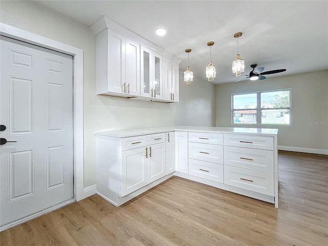 kitchen with kitchen peninsula, ceiling fan, pendant lighting, white cabinets, and light hardwood / wood-style floors