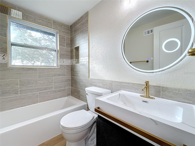 full bathroom featuring tile walls, vanity, tiled shower / bath combo, and toilet