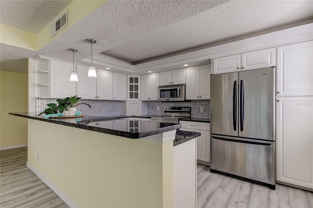 kitchen with appliances with stainless steel finishes, tasteful backsplash, light hardwood / wood-style floors, white cabinetry, and hanging light fixtures