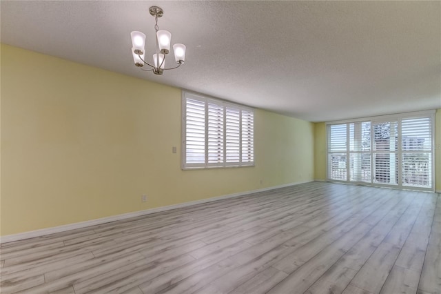 spare room with light wood-type flooring, a textured ceiling, and a chandelier