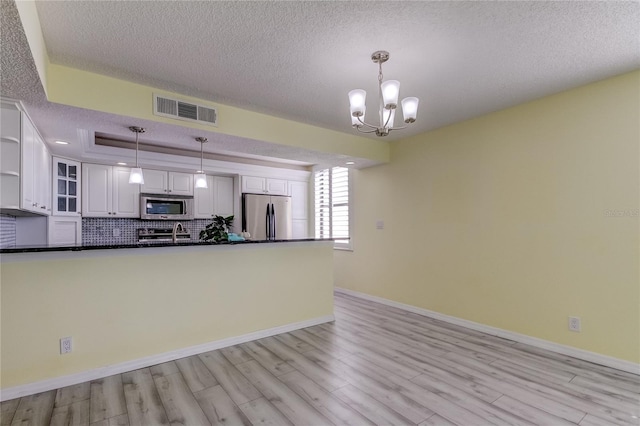 kitchen featuring a textured ceiling, stainless steel appliances, pendant lighting, light hardwood / wood-style flooring, and white cabinets