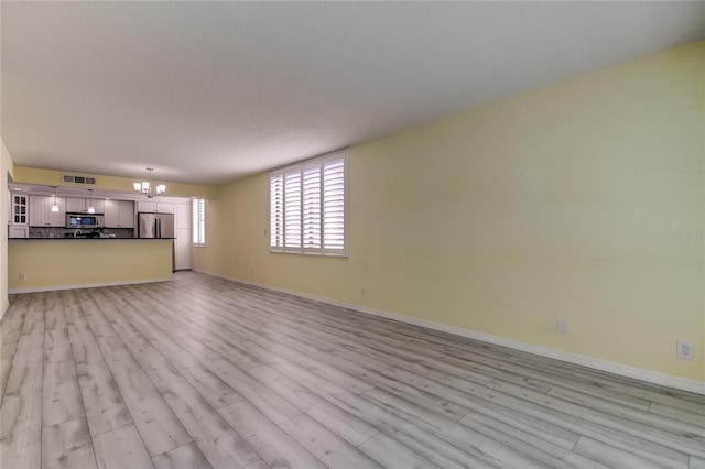 unfurnished living room with light hardwood / wood-style flooring, a textured ceiling, and an inviting chandelier