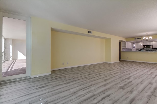 unfurnished living room with a chandelier and light hardwood / wood-style floors