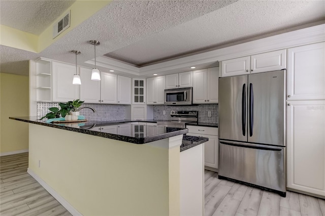 kitchen with visible vents, a peninsula, a tray ceiling, stainless steel appliances, and light wood-style floors