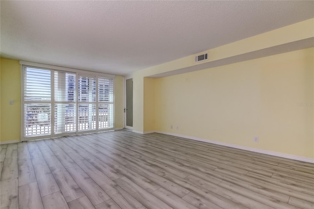 empty room with a textured ceiling, wood finished floors, visible vents, baseboards, and expansive windows