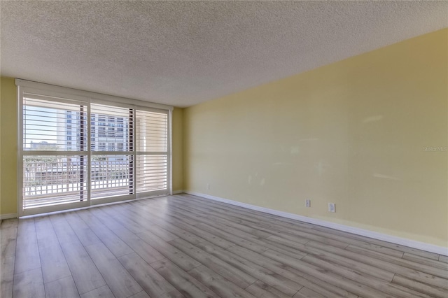 unfurnished room featuring a textured ceiling, baseboards, and wood finished floors