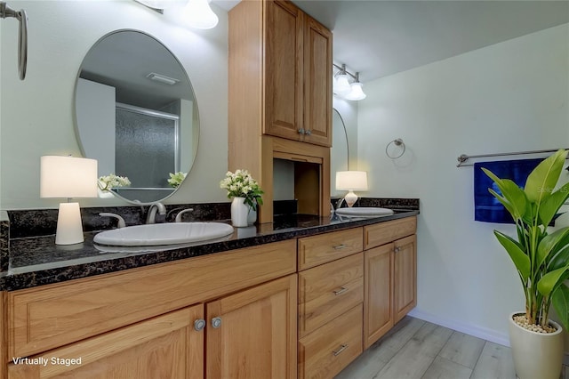 full bath featuring wood finished floors, a sink, visible vents, a shower stall, and double vanity