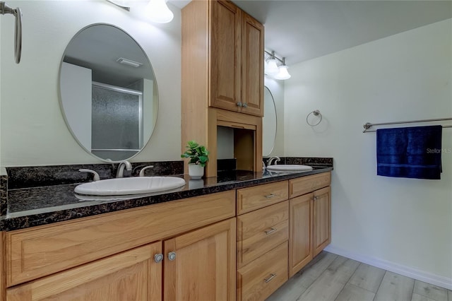 bathroom with double vanity, a sink, a shower stall, and wood finished floors