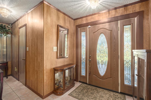 entryway with light tile patterned floors, wooden walls, a notable chandelier, ornamental molding, and a textured ceiling