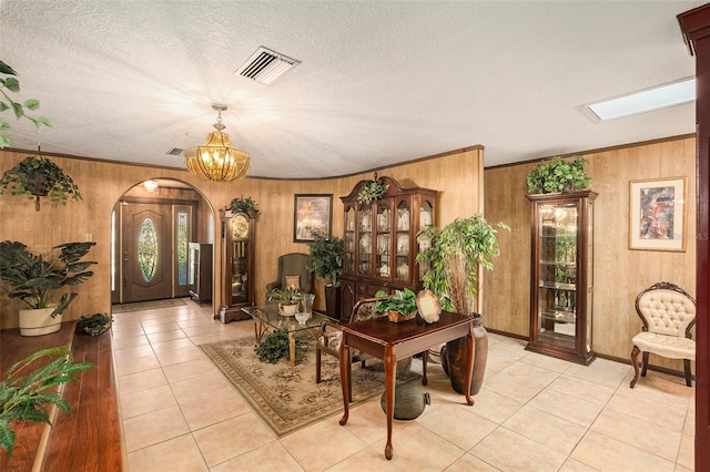 foyer entrance featuring crown molding, a skylight, a textured ceiling, light tile patterned floors, and a notable chandelier