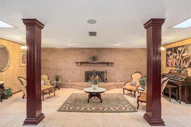 tiled living room featuring brick wall, wooden walls, decorative columns, and a brick fireplace