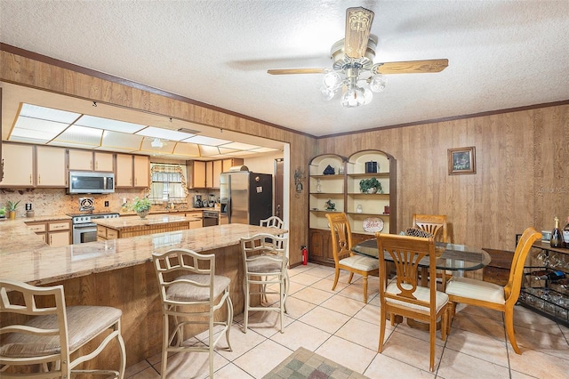 tiled dining area with ceiling fan, ornamental molding, wooden walls, and a textured ceiling