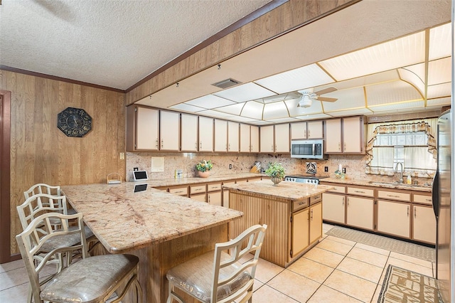 kitchen with a breakfast bar, sink, kitchen peninsula, a kitchen island, and stainless steel appliances