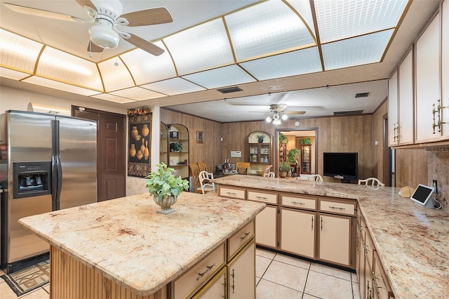 kitchen with a kitchen island, wooden walls, kitchen peninsula, stainless steel refrigerator with ice dispenser, and light stone countertops