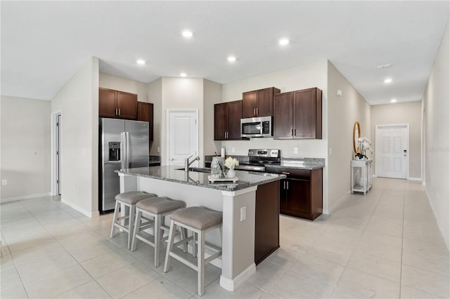 kitchen with dark stone counters, a center island with sink, sink, a kitchen bar, and stainless steel appliances