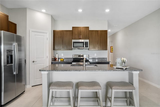 kitchen with a breakfast bar, appliances with stainless steel finishes, light tile patterned floors, and dark stone countertops