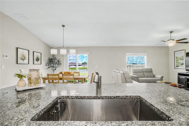 kitchen with pendant lighting, lofted ceiling, sink, and stone counters