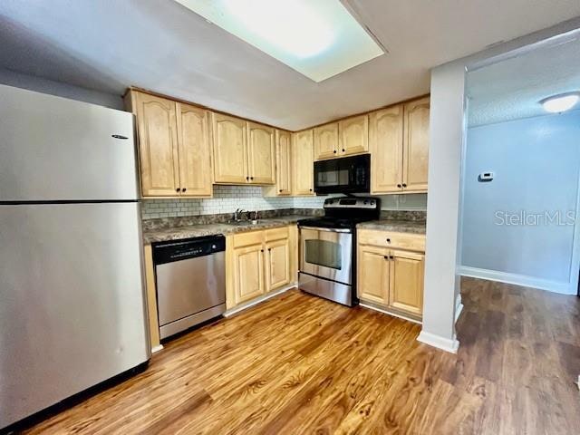 kitchen featuring decorative backsplash, wood-type flooring, stainless steel appliances, and light brown cabinetry