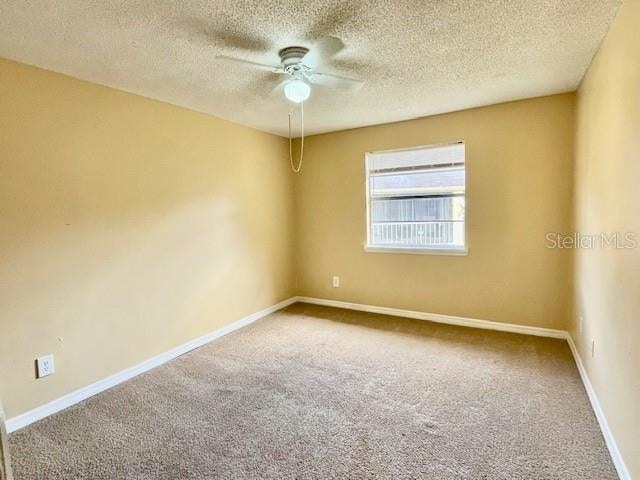 empty room with carpet flooring, ceiling fan, and a textured ceiling